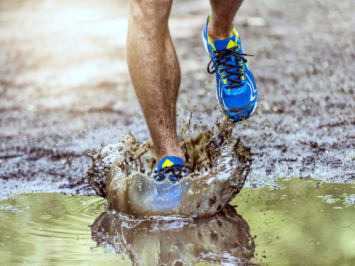Running man walking in a puddle splashing his shoes, benefits of hiking