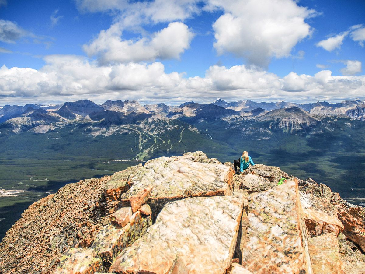 Woman sitting on top of a mountain at Mount Fairview Summit Hike in Lake Louise