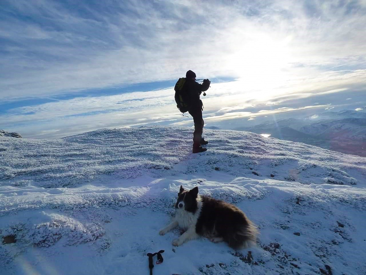 Man hiking on a snowy Blencathra peak with border collie