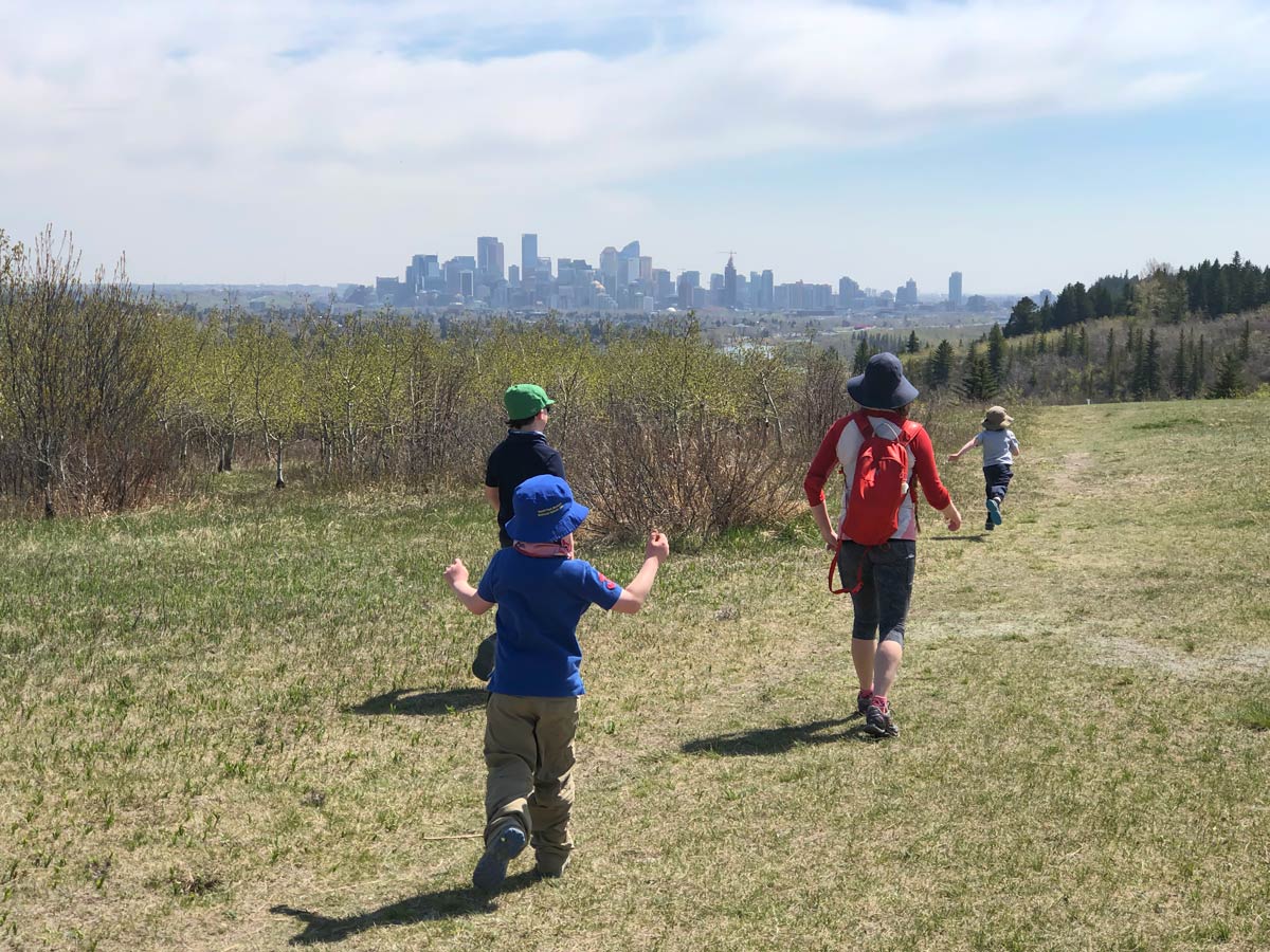 Family walking Douglas Fir Trail walking trail hills with city skyline in Calgary Alberta