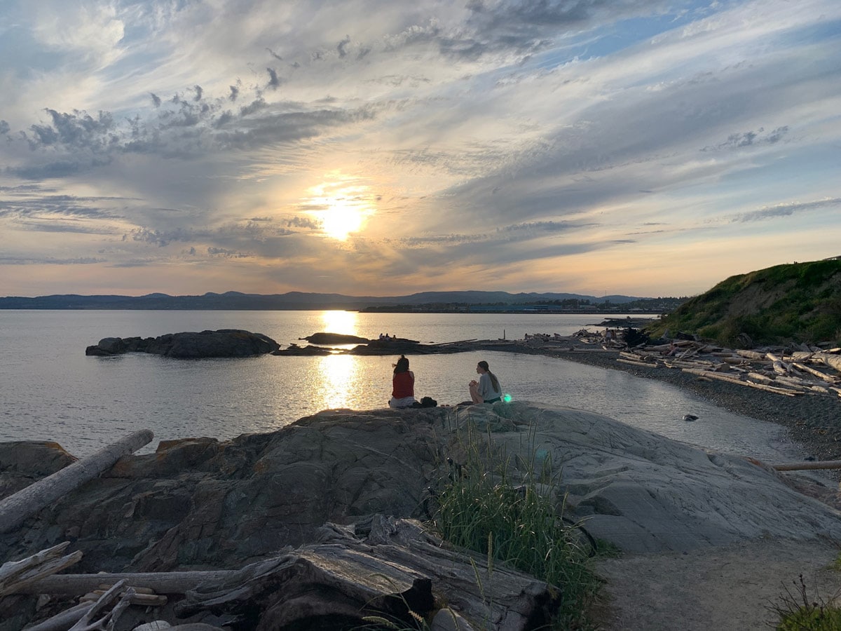 Two friends enjoy the sunset from the rock bluffs by Dallas Road near Victoria