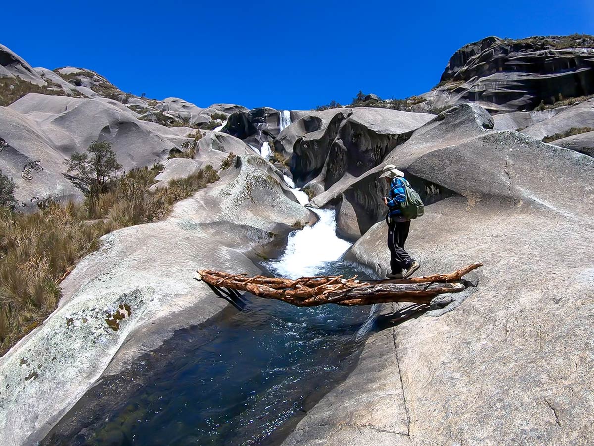 Hiker crosses river of carved rock ner Lake Auquicocha