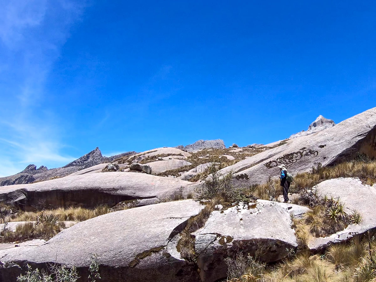 Hiker climbs over rolling rock hills on trail to Lake Auquicocha