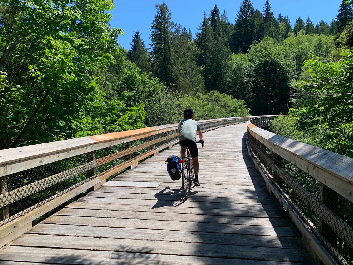 Biker traverses boardwalk through the forest along trail Goose to Sooke Potholes near Victoria