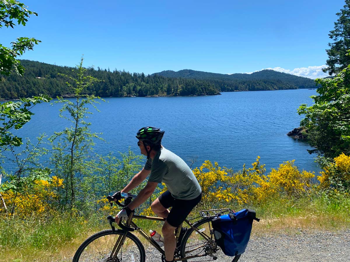 Cyclist bikes by wildflowers and ocean along Goose to Sooke Potholes trail near Victoria