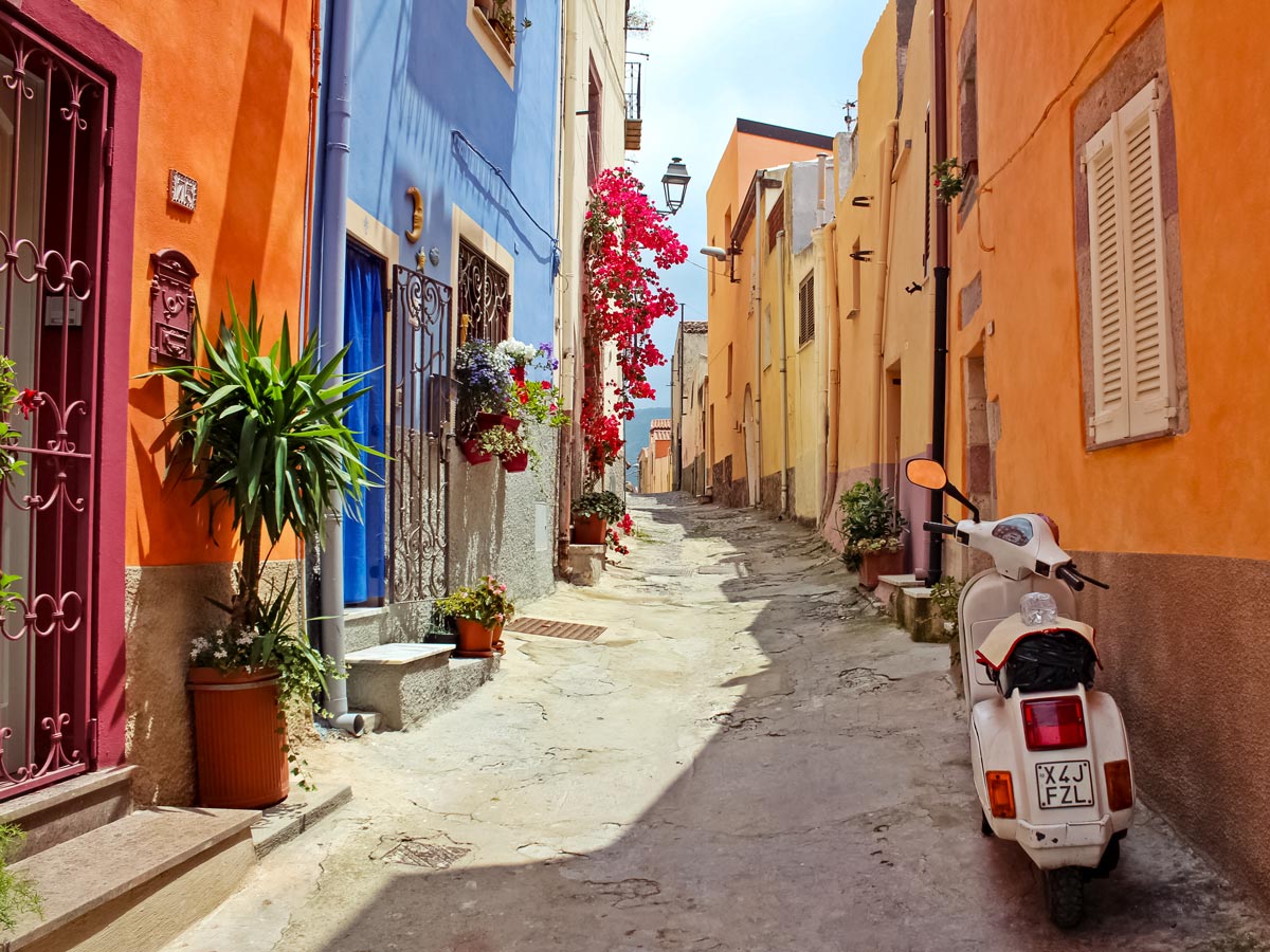 Moped bike on cobblestone street between colourful houses in italy