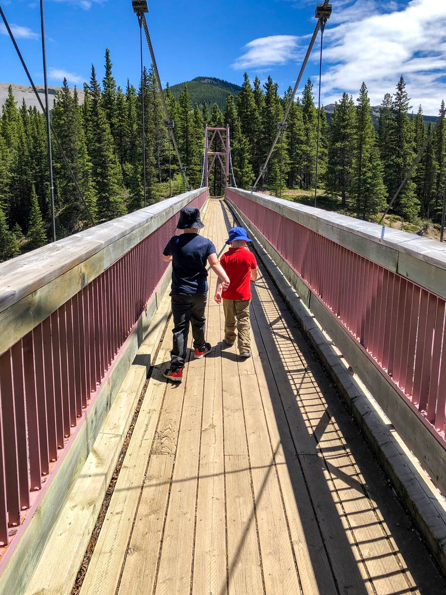 Kids crossing river bridge along Little Elbow hiking trail Kananaskis Alberta Canada