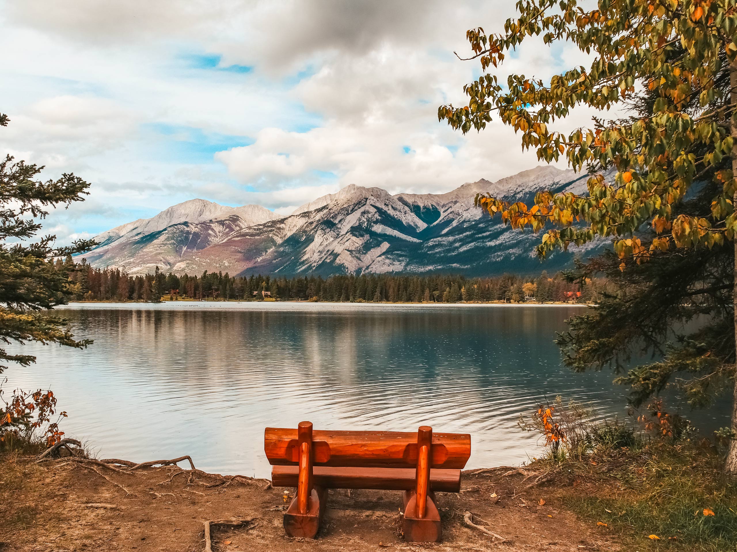Wooden bench on lake shore overlooking Lake Edith and mountains in background hiking Jasper Naitonal Park