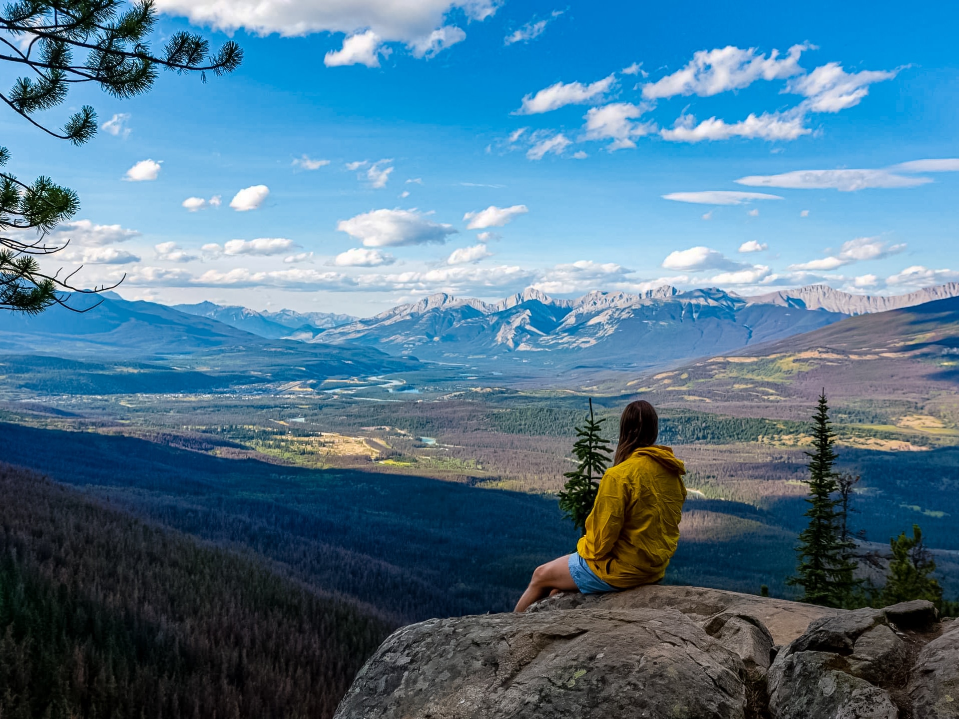 Hiker sitting on rock looking out over valley river below Jasper