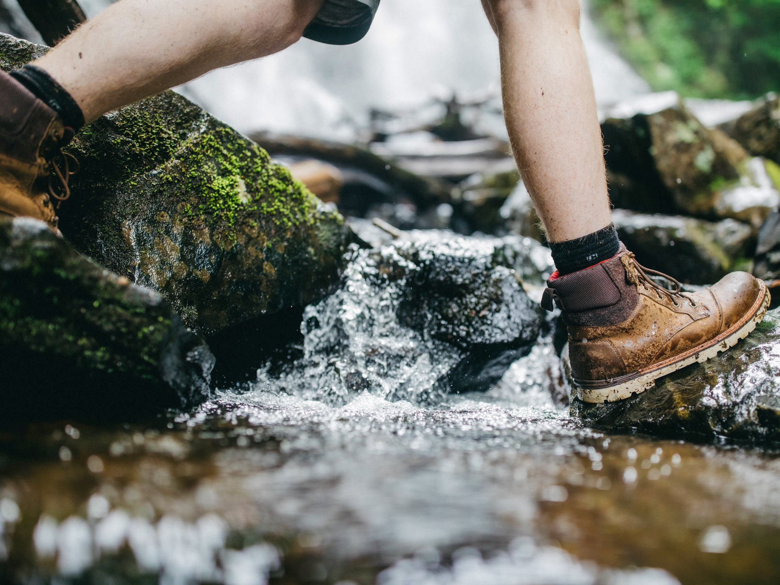 Hiking boots on mossy rocks crossing stream creek